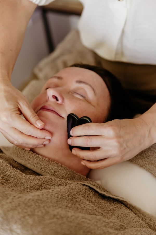 A woman enjoying a facial massage with a black gua sha tool.
