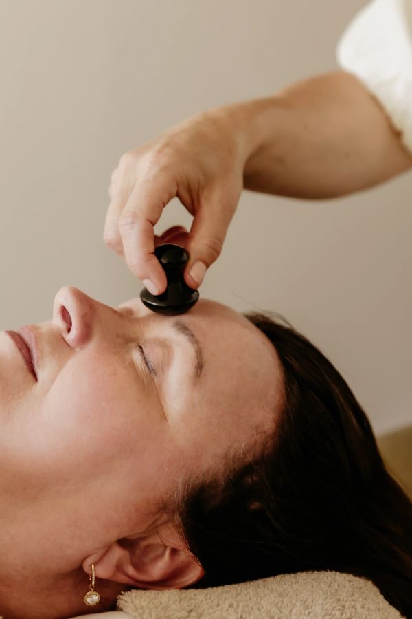 Person receiving facial massage with a black stone tool.