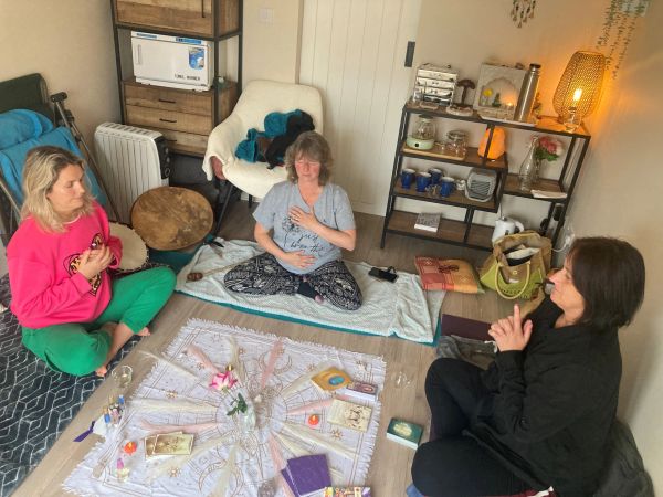 Three women meditating around a cloth with crystals and books.
