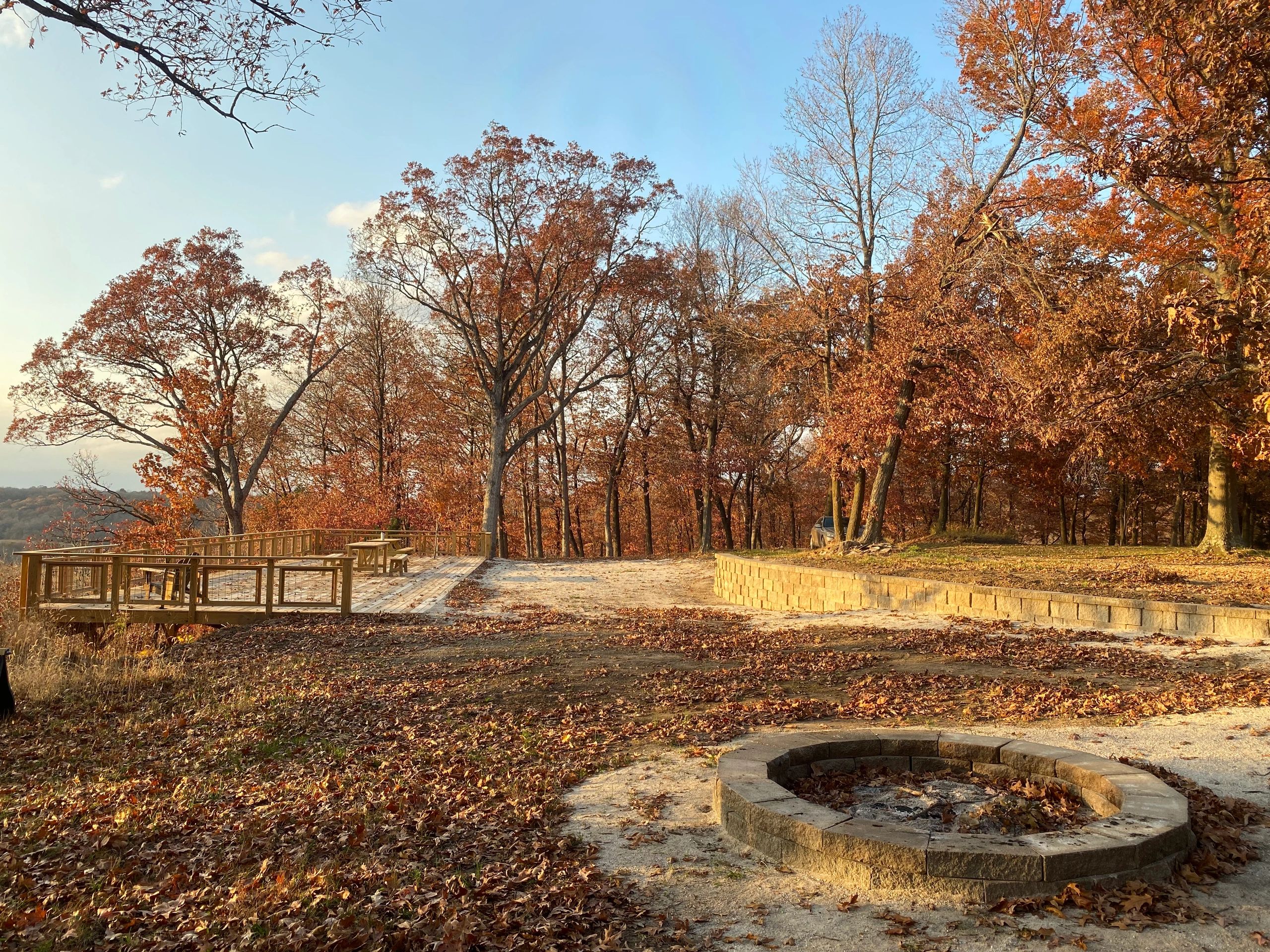 Autumn scene with orange leaves, a fire pit, and a wooden deck under clear skies.