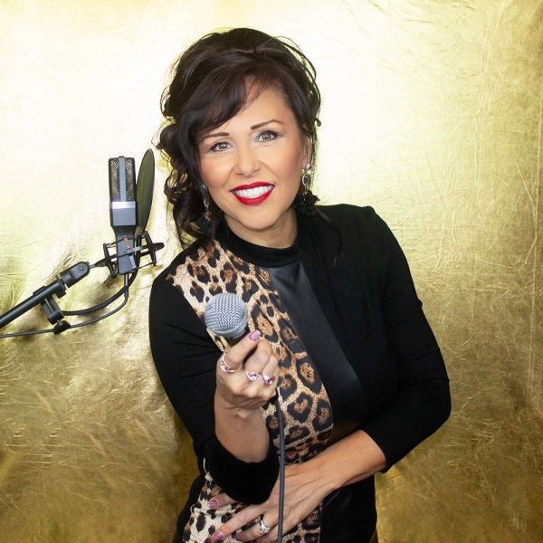 Woman smiling and holding a microphone in front of a golden backdrop.