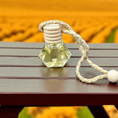 A small glass bottle with a rope on a wooden surface against a blurred yellow flower field.