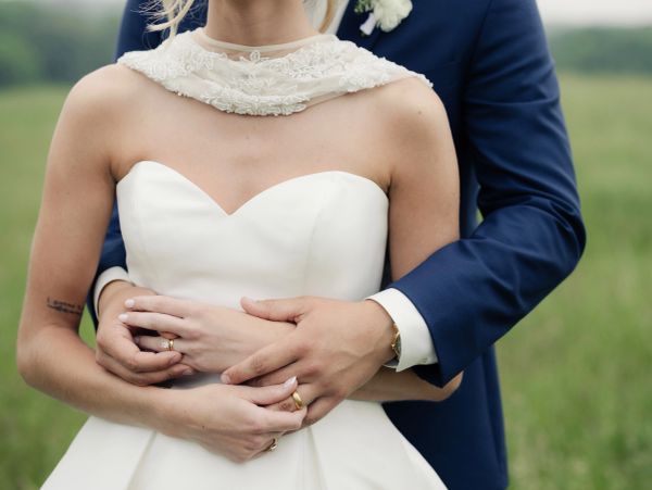 Newlyweds embracing outdoors, showing wedding rings.