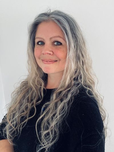 Smiling woman with long wavy gray hair and blue eyes.