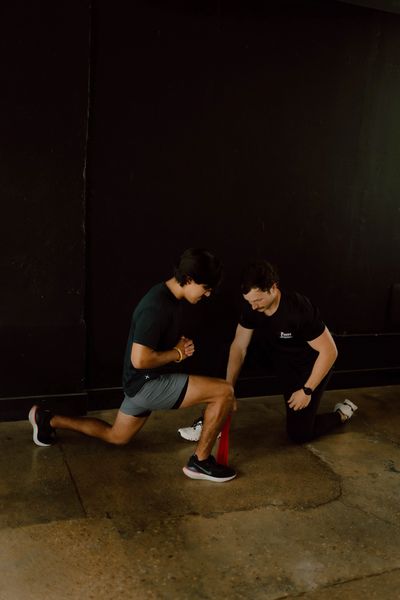 Chiropractor assisting a man with resistance band exercise in a gym.