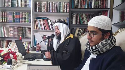Two men in traditional attire reading religious texts in a library setting.