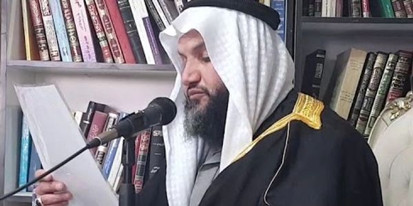 Two men in traditional attire reading and speaking in a library.