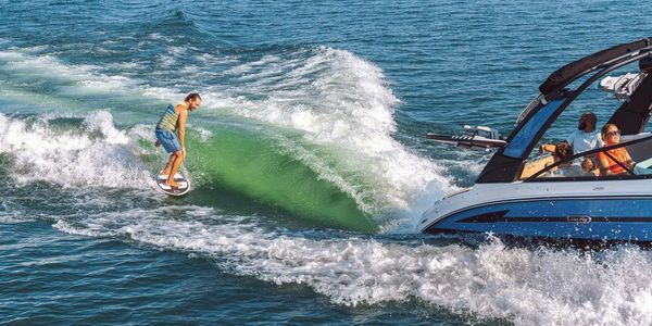 A man wakesurfs behind a motorboat on clear water.