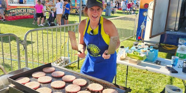 Woman cooking burgers on a grill at outdoor event.