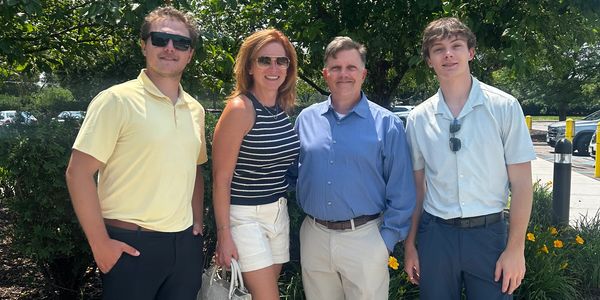 Four people casually posing outdoors on a sunny day.