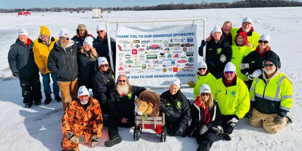 Group of people posing in snow around a sponsor banner.