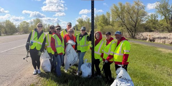 Group of people in safety vests holding trash bags during cleanup.