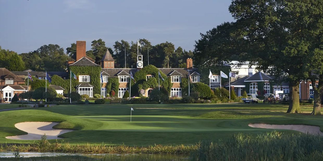 Scenic golf course with a clubhouse and green surrounded by trees and flags.