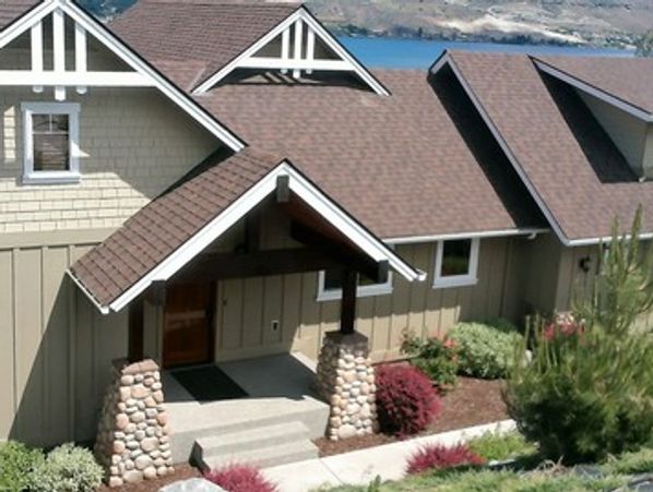 A modern house with a brown roof and stone pillars at the entrance.