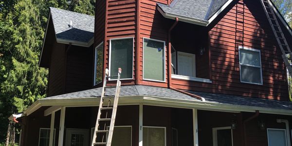 A red two-story house with a turret and ladders set up for painting or maintenance.