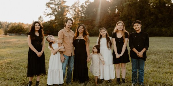 A family of eight standing in a sunlit field during golden hour.