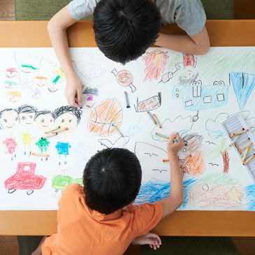 Dos ninos sentados en una mesa pintando y coloreando 