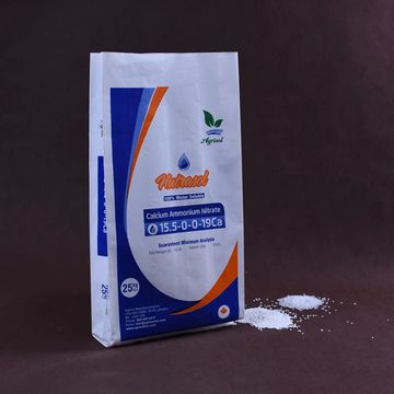 Bag of calcium ammonium nitrate fertilizer with some spilled on surface.
