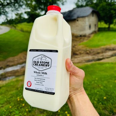 Hand holding a gallon of Old Stone Creamery whole milk outdoors.