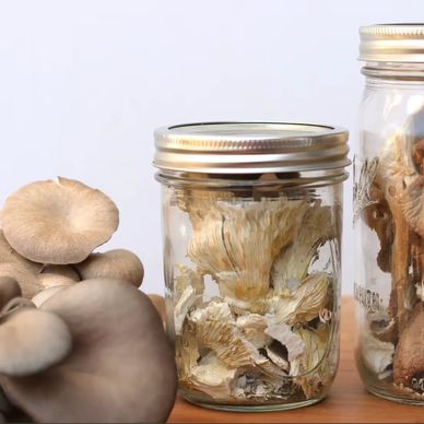 Jars filled with dried mushrooms beside fresh mushrooms on a wooden surface.