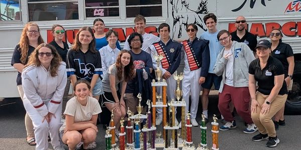 Group of people posing with multiple trophies in front of a bus.