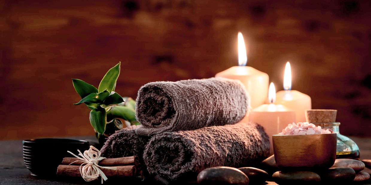 Relaxing massage atmosphere. Candlelight behind spa towels. Hot Stones and salt scrub supplies.