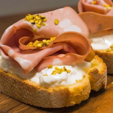 Pan campesino tostado, con crema de burrata, mortadella y nueces frescas desmenuzadas.