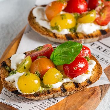 Pan campesino tostado, una capa de pesto genovés, otra capa de crema de burrata y tomates cherry.