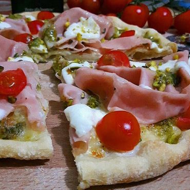 Suave  focaccia, con una capa de pesto, mortadella, tomates cherry, chispas de burrata y nueces.