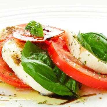Primer plano de una ensalada Caprese con tomates rojos en rodajas, mozzarella, hojas de albahaca.