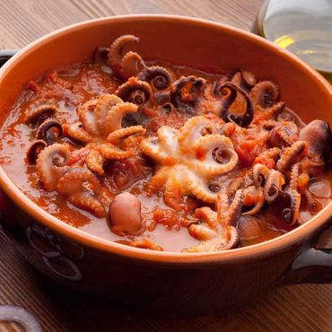 Un tazón humeante de estofado de pulpo en una rica salsa de tomate, con aceitunas.