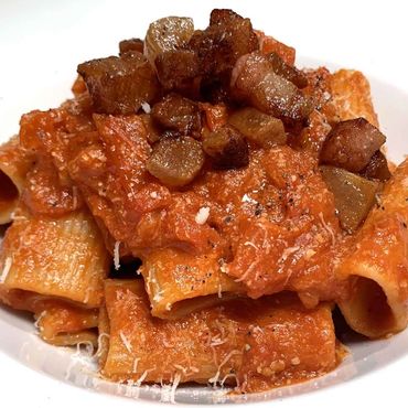 Plato de rigatoni a la Amatriciana con salsa de tomate y guanciale.