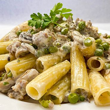 Plato de rigatoni a la Boscaiola con guisantes, salchicha y champiñones en salsa de aceite y ajo.