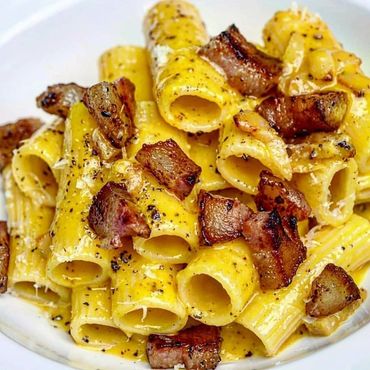 Plato de rigatoni a la carbonara con guanciale y pimienta negra sobre un plato blanco.