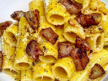 Plato de rigatoni a la carbonara con guanciale y pimienta negra sobre un plato blanco.