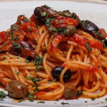 Plato de espaguetis a la puttanesca con salsa de tomate, aceitunas y alcaparras