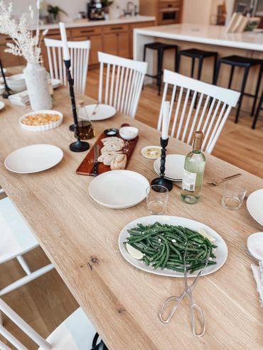 Elegant dining table with green beans, bread, candles, and wine in a modern kitchen.