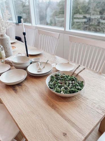 A wooden dining table set with white plates and a bowl of fresh salad.