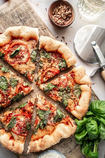 pizza with tomatoes and spinach on wood cutting board with pizza cutter and fresh basil made by Chic