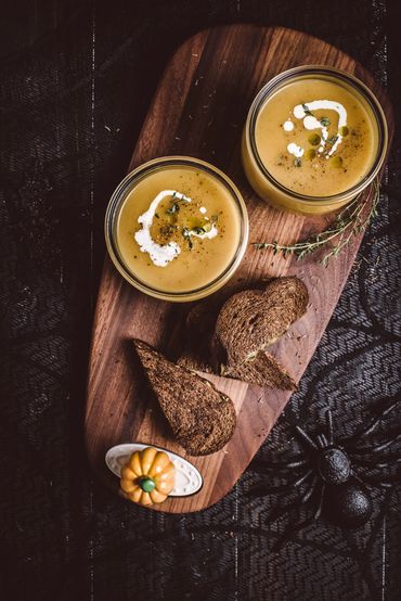Two bowls of creamy pumpkin soup with bread on a wooden board.