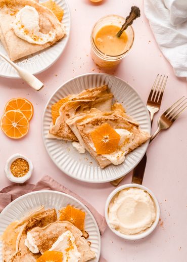 orange crepes on three different plates on pink background made by Chicago Food Stylist Nicole Trieb