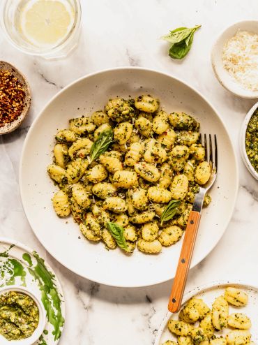 Plate of gnocchi with pesto sauce and basil leaves.