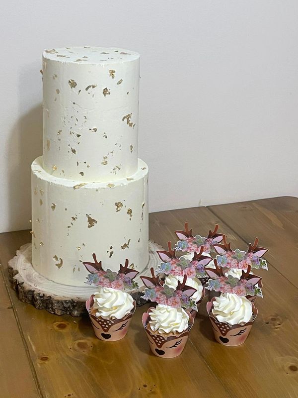 Two-tier white cake with gold flakes and deer-themed cupcakes.
