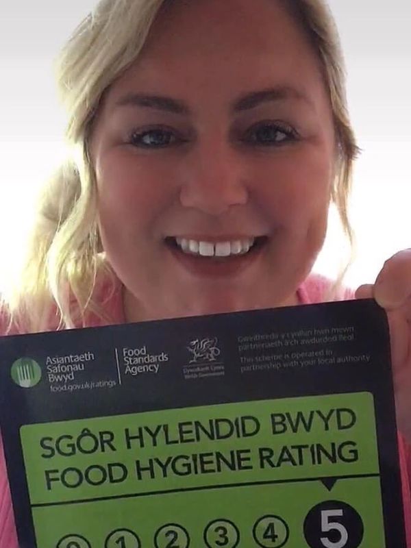 A woman smiles holding a food hygiene rating sign with a top score of 5.