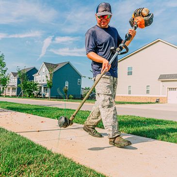 Man using a string trimmer on sidewalk edge.