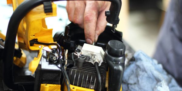 Hand repairing a yellow chainsaw engine.
