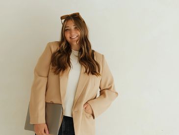 Smiling woman with a beige blazer and sunglasses on her head.