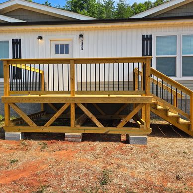 Newly built wooden deck attached to a white house with stairs and railings.