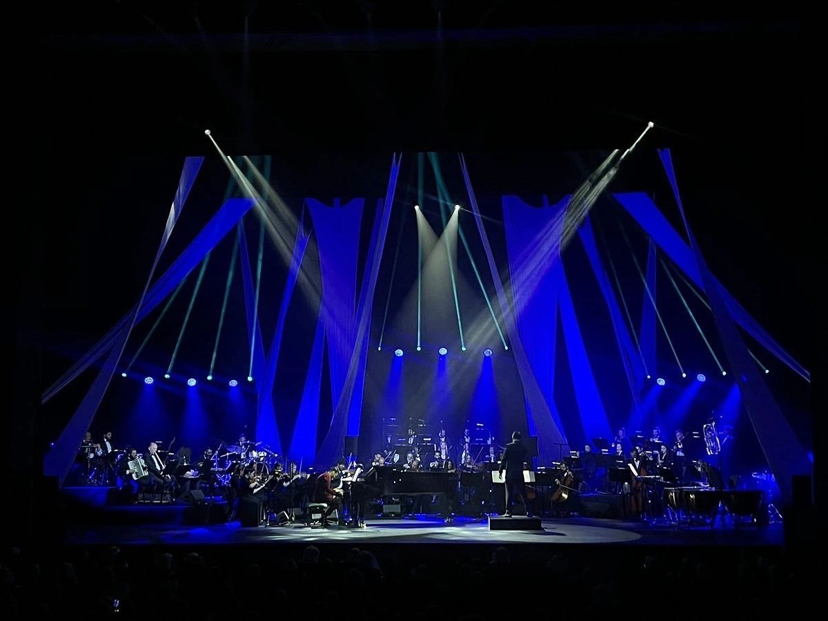 Symphony orchestra performing on stage with blue lighting and conductor.