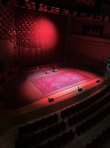 Empty concert hall stage illuminated by red light with a decorative carpet.